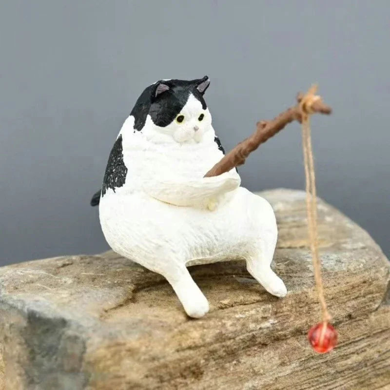 Cat-shaped figurine holding a fishing rod with a red bobber on a rock against a gray background