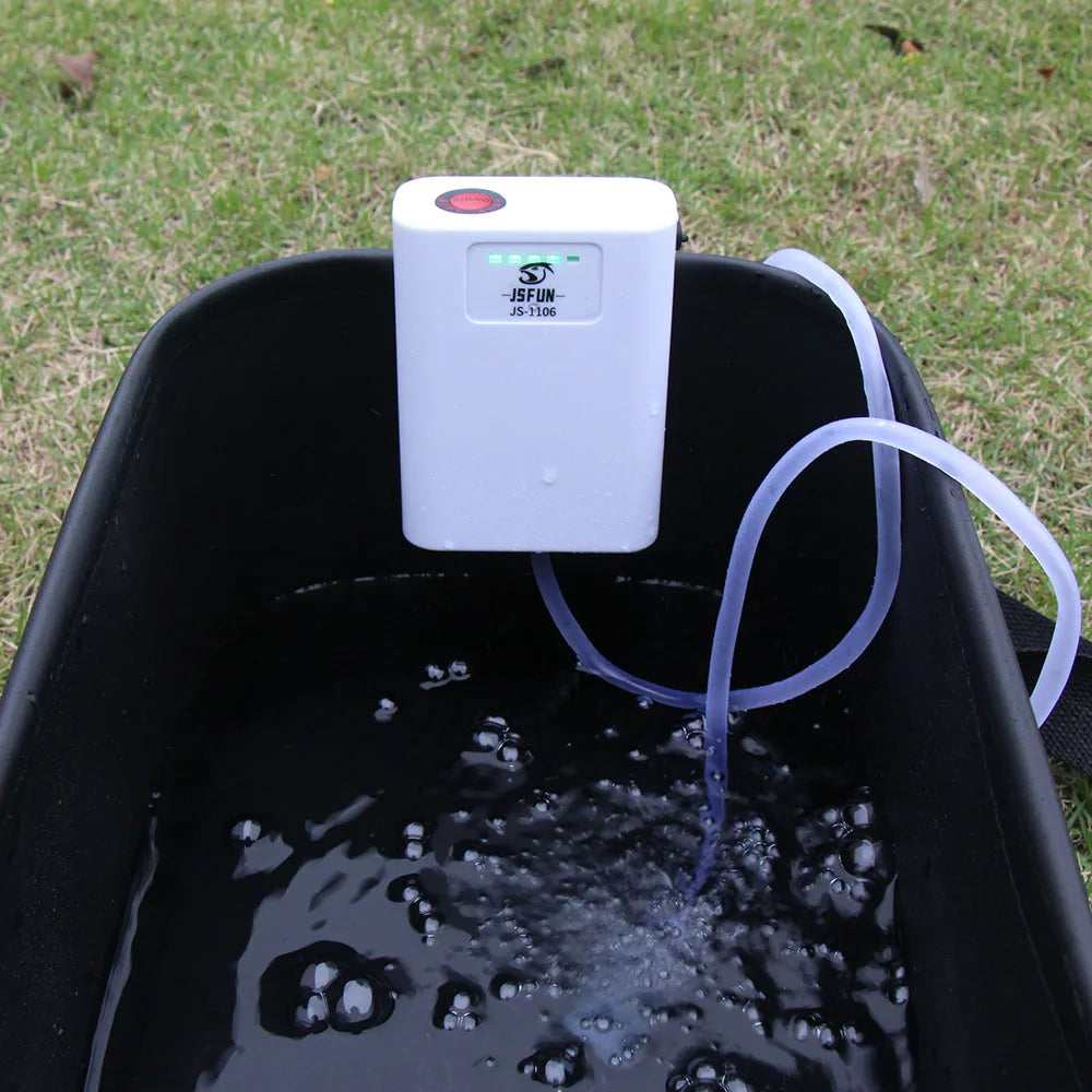 White electronic device with a red light on top of a black container filled with water, connected to a hose.