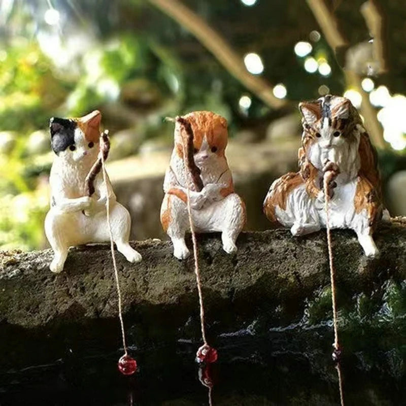 Three miniature cat figurines sitting on a branch with a blurred natural background