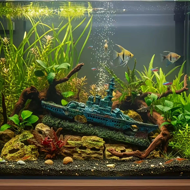 A beautifully arranged freshwater aquarium featuring a blue toy battleship decoration on a rocky base, surrounded by lush green aquatic plants, driftwood, and small fish swimming in the water.